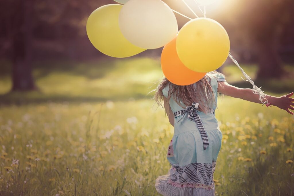 Girl running through sunlit field with balloons